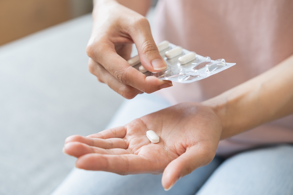 a person is holding a pill packet and dispersing a single pill for them to take from a packaged course of antibiotics.